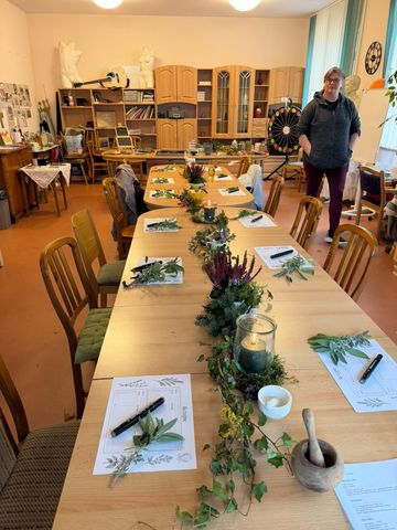 Lange gedeckte Tafel mit Rezeptbögen, Stiften, frischen Kräuterzweigen, Heidekraut und Windlichtern